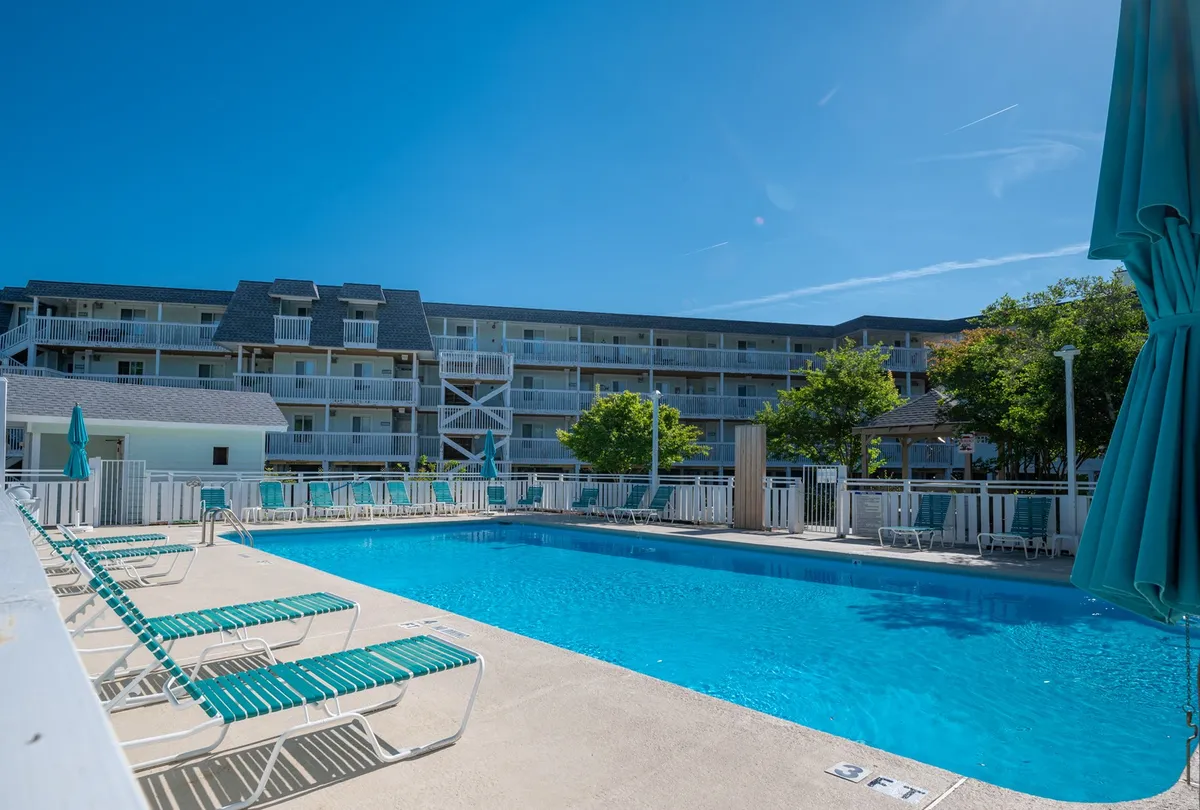 This image captures an inviting outdoor swimming pool surrounded by lounge chairs and umbrellas, with the facade of the building and well-maintained landscaping in the background. The scene suggests a leisurely, resort-like atmosphere perfect for relaxation or socializing.