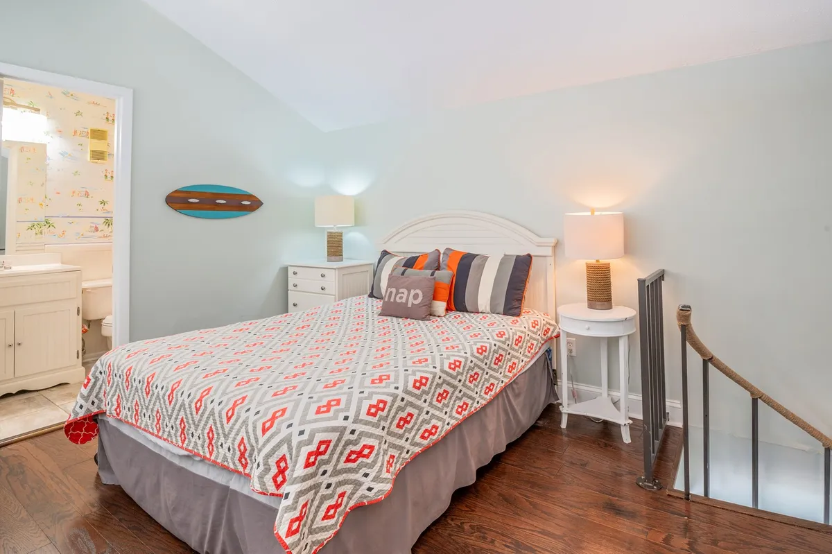 A cozy bedroom with decorative pillows, ambient lamps, and a staircase in the background. The environment feels restful and welcoming, perfect for unwinding after a busy day. The staircase suggests access to additional private spaces, likely referencing the loft area.