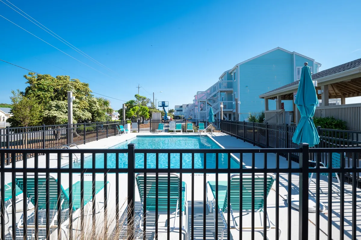 This image shows a vibrant outdoor swimming pool area surrounded by lounge chairs, shade umbrellas, and pedestrian pathways. The scene conveys a sense of leisure and is clearly designed for family use, with plenty of space for relaxing and playing together.