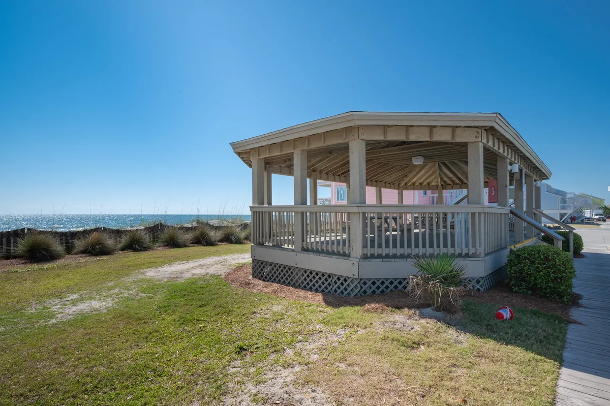 This image displays a gazebo structure overlooking a beautifully landscaped grassy area with the ocean visible in the background. The scene is set for outdoor relaxation, group gatherings, or enjoying a quiet coffee while taking in the sea breeze.
