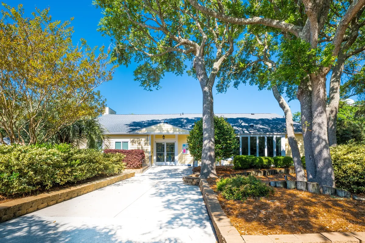 The photo shows the condo’s front entrance surrounded by a lush, landscaped garden and large trees. The inviting outdoor space hints at a peaceful environment ideal for family or friends to gather before or after local adventures.