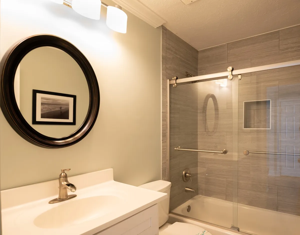 A serene bathroom scene with a mirror, shower area, and stylish sink. Clean lines and tranquil lighting emphasize a spa-like, rejuvenating atmosphere.