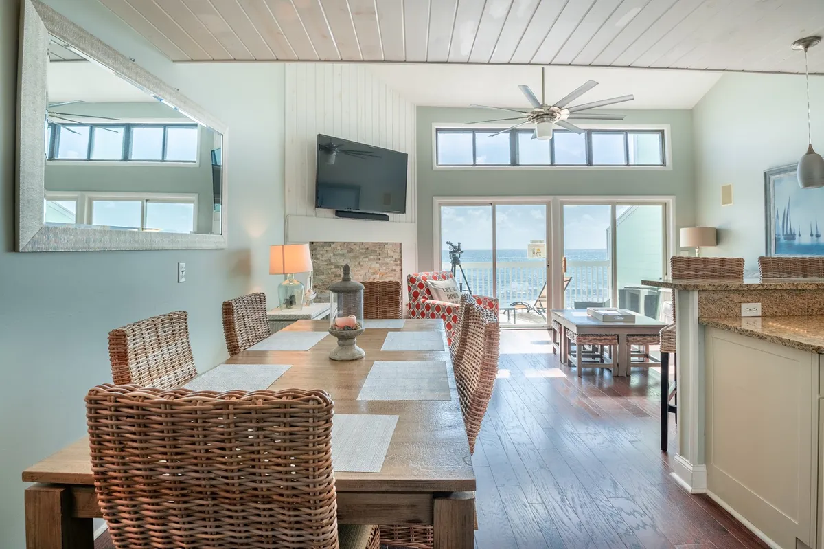 This image features a spacious open-plan living, dining, and kitchen area with a dining table, sofa seating area, and large windows offering an ocean view. The setup is ideal for family dinners, relaxing with a view, or social gatherings, and showcases how natural light fills the space.