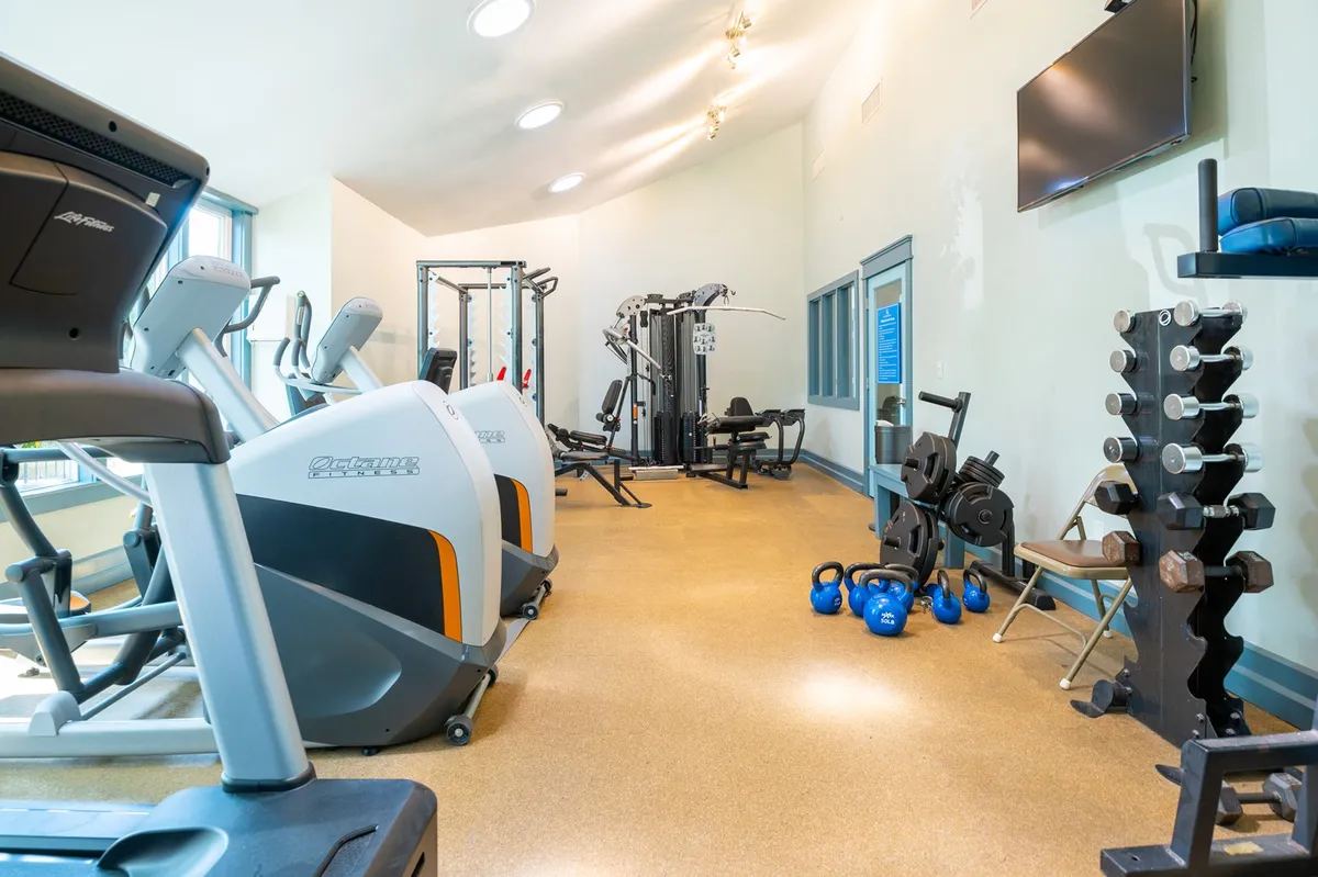 A well-equipped fitness center featuring treadmills, weight machines, free weights, exercise mats, and a mounted television. The space is bright and energetic, inviting guests to pursue their fitness goals.