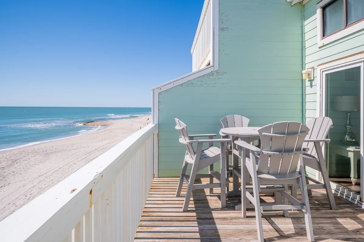 An inviting scene featuring an outdoor dining set on a sundeck overlooking the ocean. The sea horizon is visible, and the deck is an ideal spot for relaxing or enjoying a meal while listening to the waves and soaking in the ocean breeze.