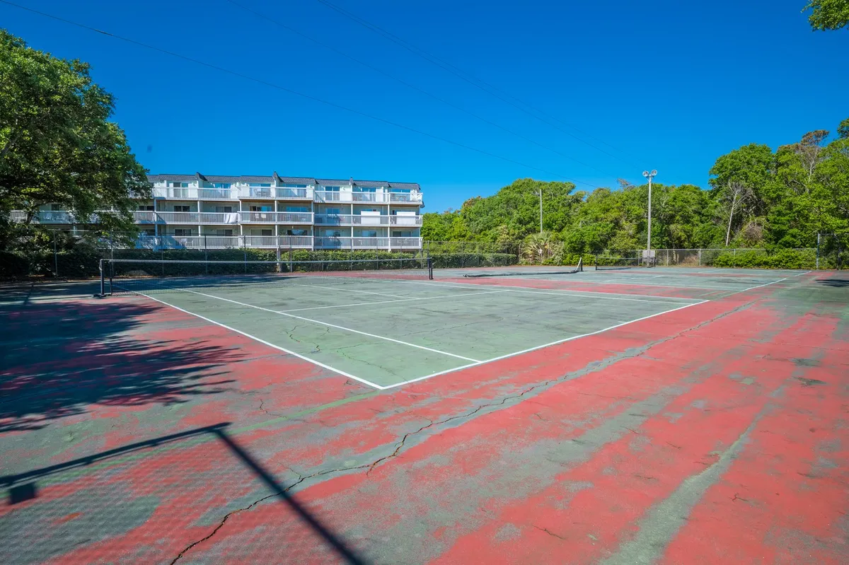 A vibrant tennis court surrounded by greenery with a residential building in the background. The scene highlights space for active recreation and social matches in a lively, outdoor setting.