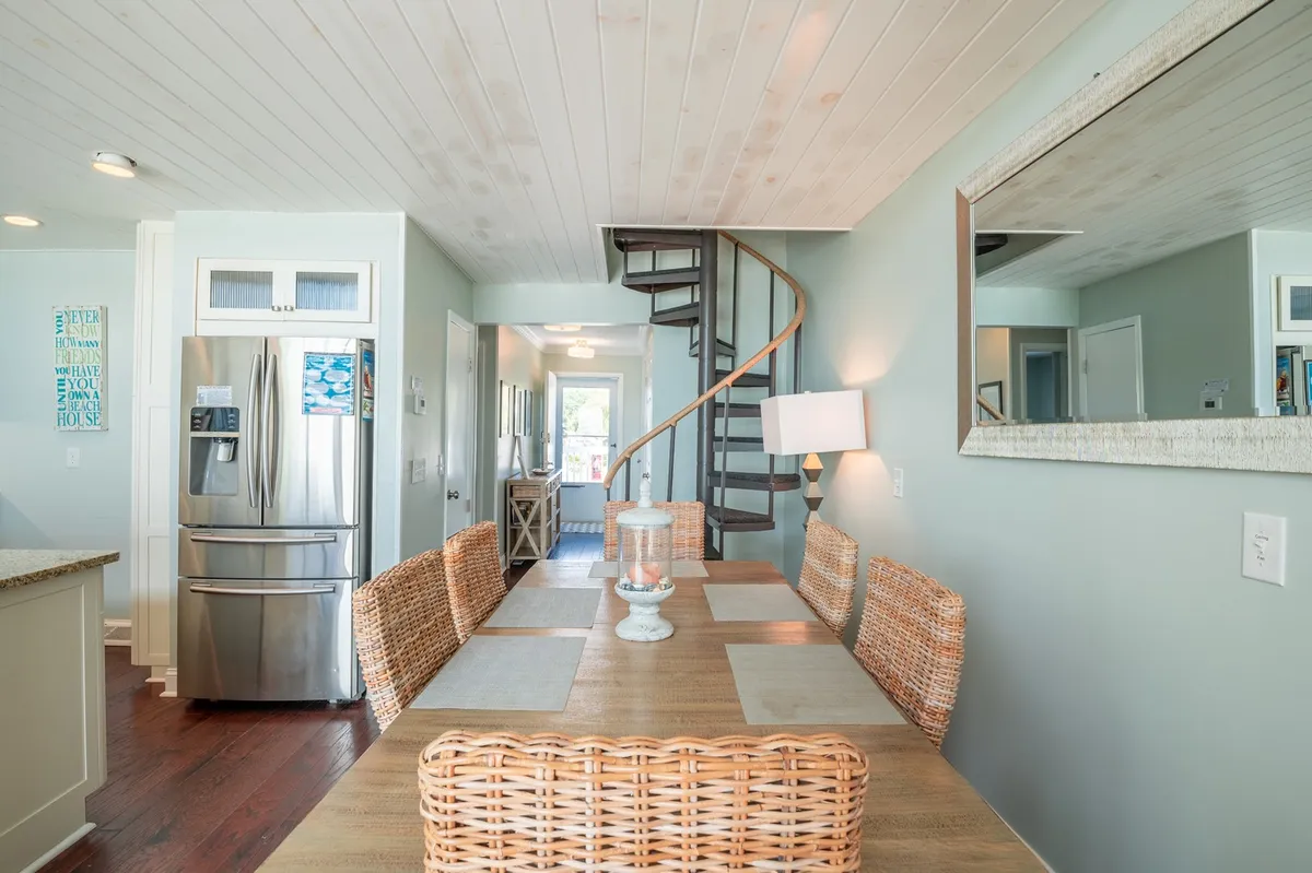 A welcoming dining area anchored by a striking spiral staircase, with a table set for gatherings and glimpses of the kitchen. The spiral staircase is a distinct architectural focal point, leading upward toward the loft area.
