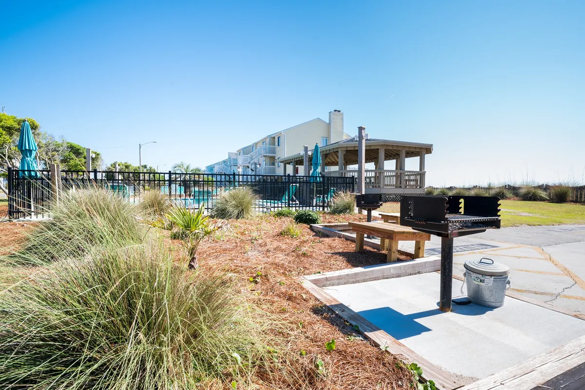 A lively outdoor grill area near a swimming pool, featuring a picnic table, lounge chairs, and landscaped grass. The space is designed for group gatherings, barbecues, and family picnics, emphasizing active and social resort life.