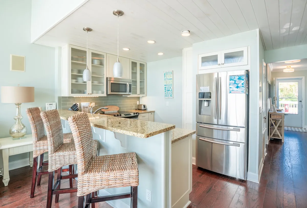 The kitchen area is highlighted here, with a granite countertop, bar stools, stainless steel appliances, and stylish light fixtures. The modern design and attention to detail are evident, making it a focal point for cooking and socializing.